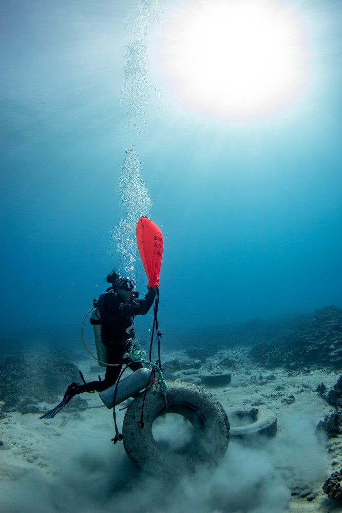 a scuba diver fills a lift bag to remove a tire from underwater